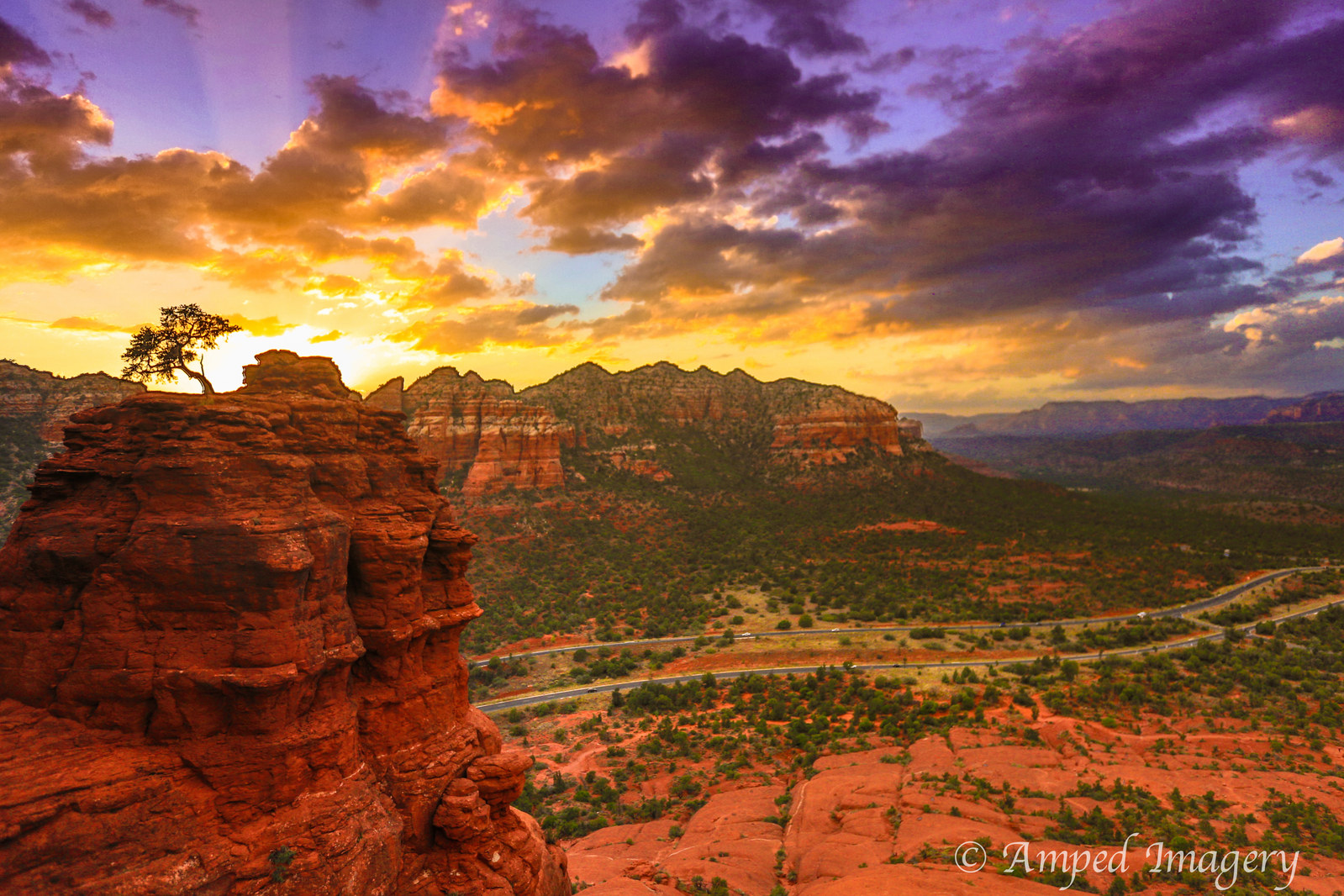 Sunset across red-rock cliffs and a lone tree beneath a dramatic sky